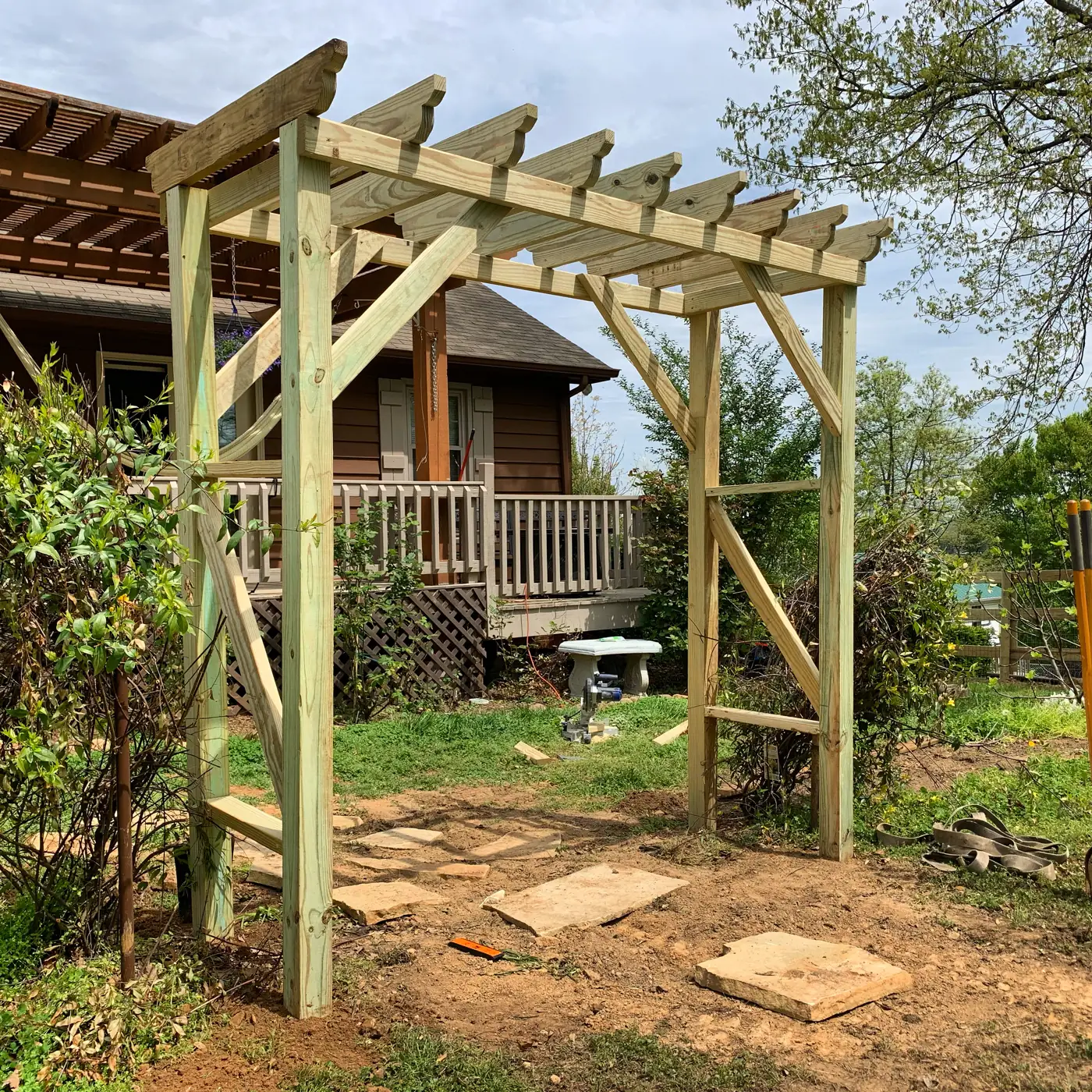 Open rafters and posts of a wood pergola over a stone path